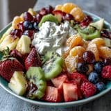Vibrant rainbow fruit platter with coconut whipped cream, perfect for healthy brunch or party dessert.