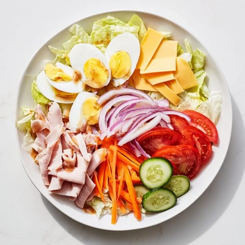A hearty American Chef Salad topped with quartered hard-boiled eggs, tomato wedges, cucumber, and crunchy julienned carrot.