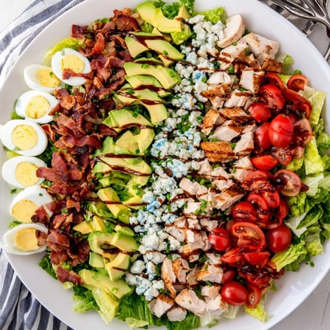Colorful, layered Cobb Salad on a platter featuring tender chicken, smoky bacon, hard-boiled eggs, and creamy avocado, drizzled with a tangy vinaigrette for a fresh American dinner.