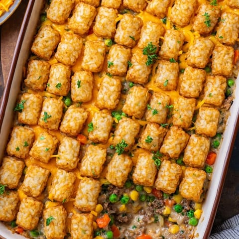 A hearty scoop of baked Tater Tot Casserole served on a plate with a fresh green salad.