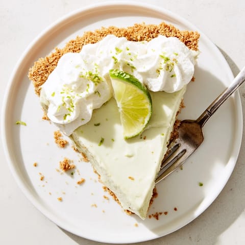 A chilled slice of Key Lime Pie topped with fluffy whipped cream and a sprinkle of lime zest.