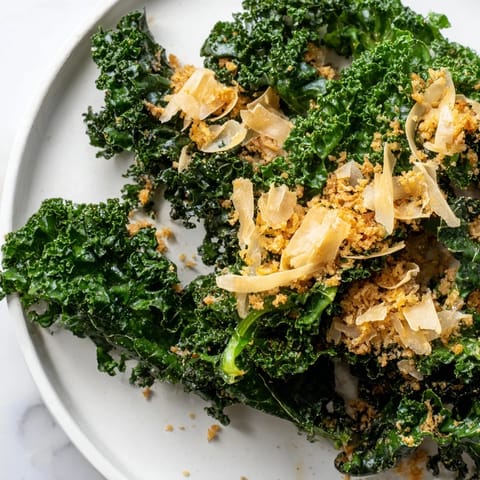 A vibrant bowl of Garlic Parmesan Kale Salad, garnished with shaved Parmesan and fresh cracked pepper, served as a light lunch.