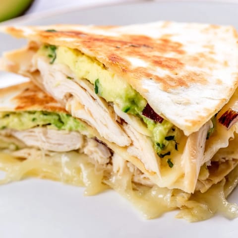 Juicy grilled chicken and creamy avocado mash tucked inside a golden-brown Chicken Avocado Quesadilla, served warm with fresh cilantro and a lime wedge.