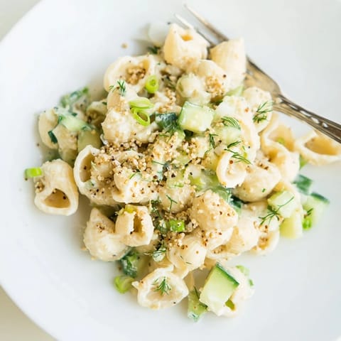 A close-up view shows diced cucumbers, green onions, and dill mixed into small shells, all topped with everything bagel seasoning. 