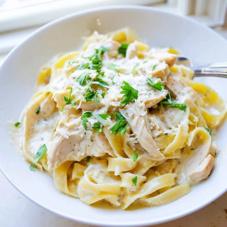 Steaming Fettuccine Alfredo in a white bowl, rich Parmesan sauce coating every strand beautifully.