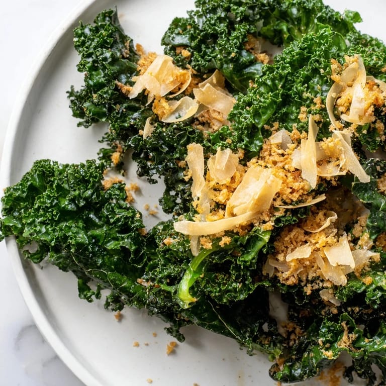 A vibrant bowl of Garlic Parmesan Kale Salad, garnished with shaved Parmesan and fresh cracked pepper, served as a light lunch.
