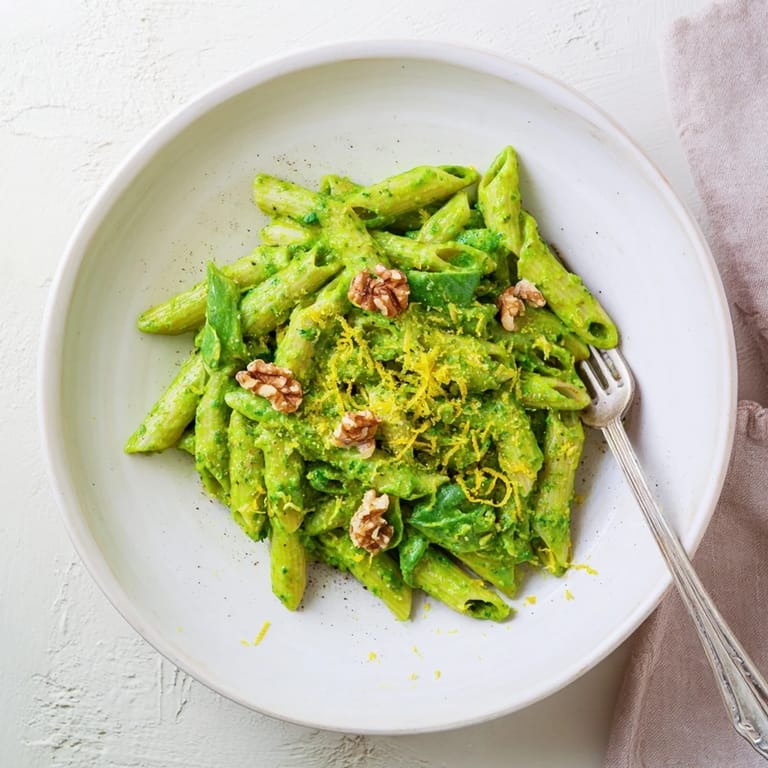 A bowl of vegan creamy spinach walnut pasta served warm, with toasted walnuts and a drizzle of olive oil on top.