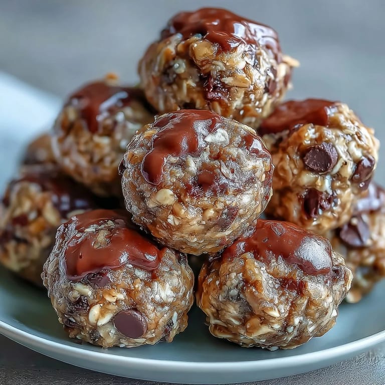 A hand holding a Banana Chocolate Chip Energy ball, ready to eat, with a gooey chocolate chip center and a sprinkle of sea salt on top.