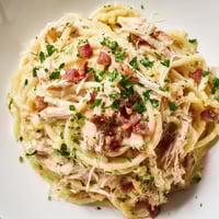 Creamy Chicken Carbonara pasta twirled on a fork, topped with crispy bacon bits and fresh parsley garnish.
