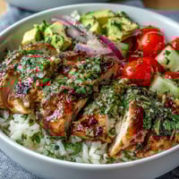 Golden grilled chimichurri chicken slices rest on fluffy rice with diced cucumber, cherry tomatoes, and creamy avocado slices.